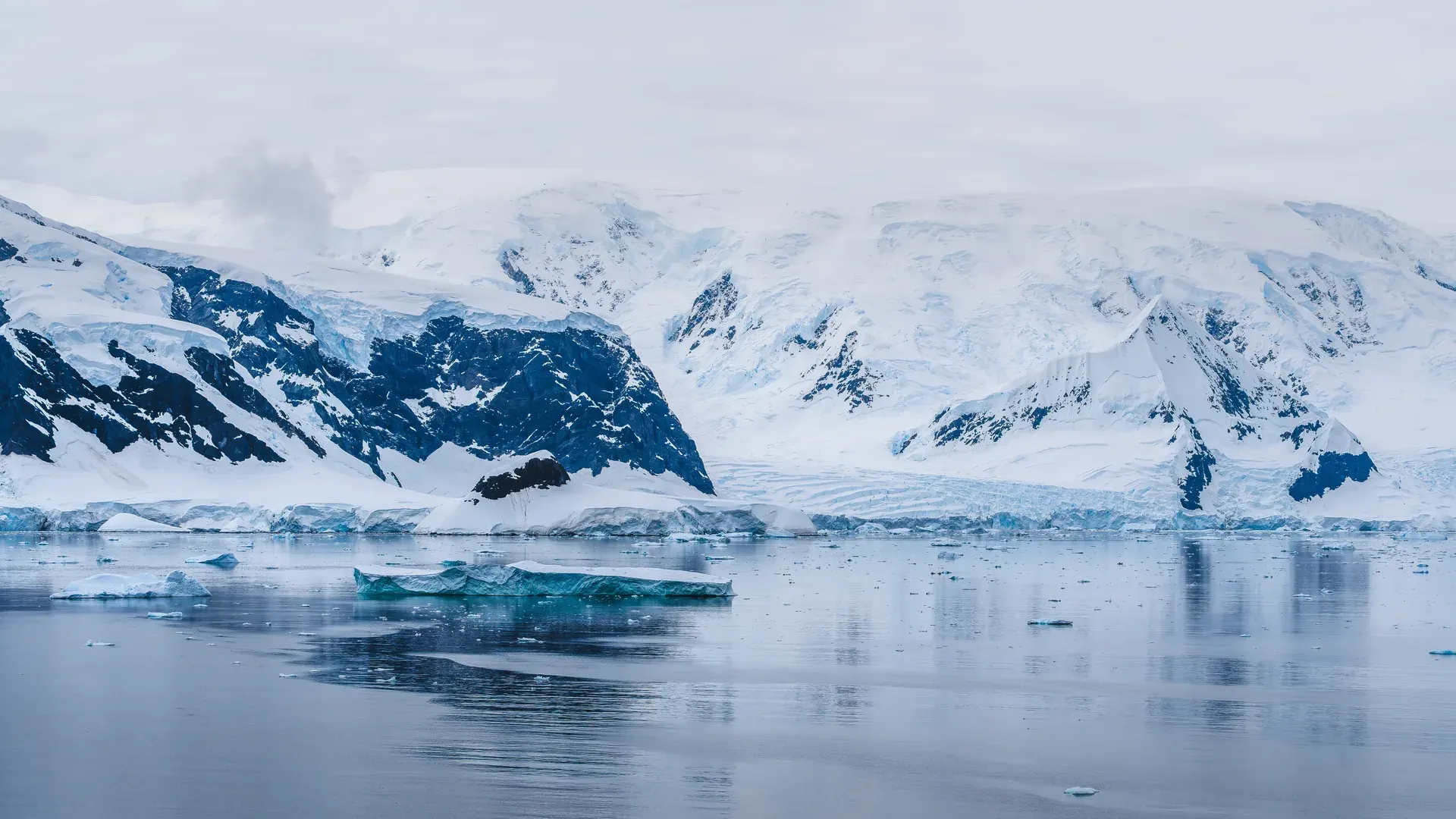 Un témpano bajo flotando en agua quieta frente a un frente de glaciar y montañas nevadas