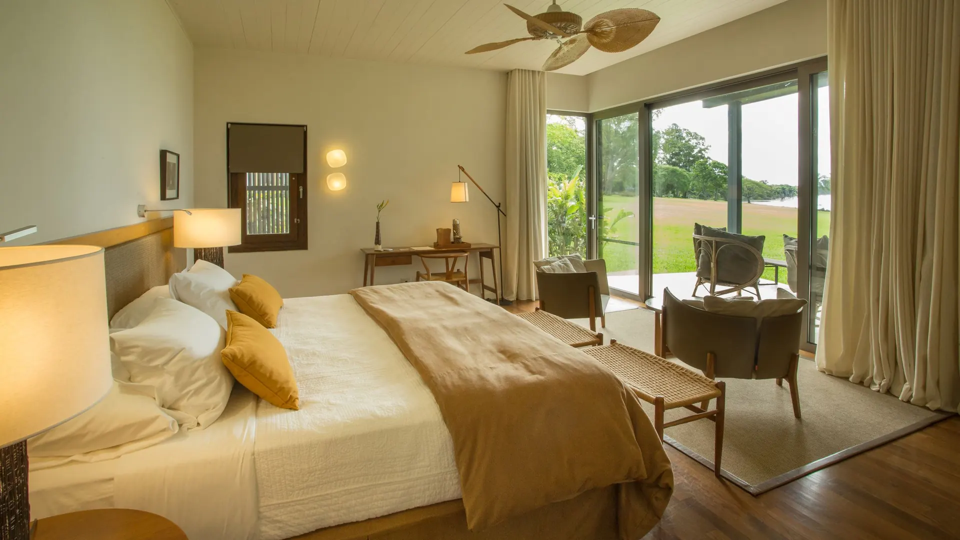 Habitación Deluxe con la cama frente al ventanal, la terraza y el parque hasta el río